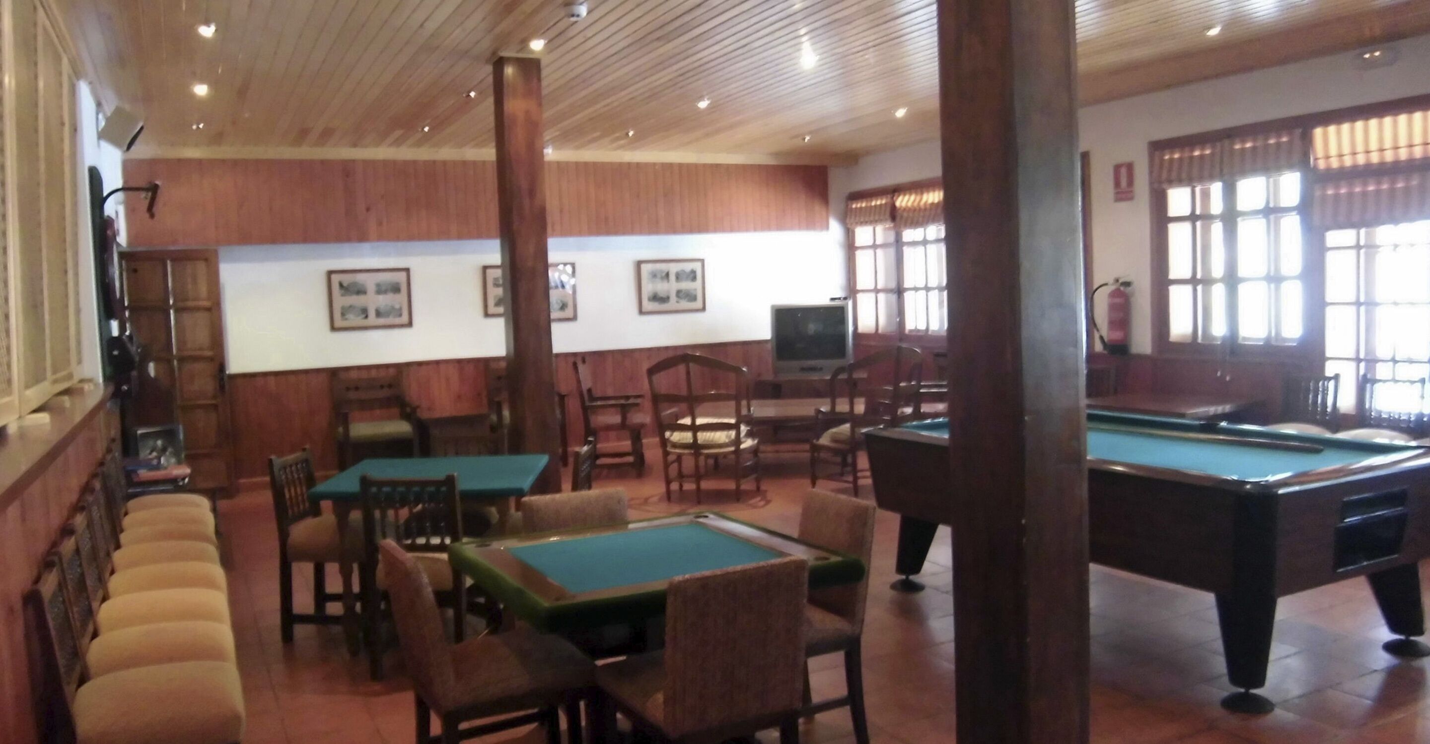 Une salle de billard dotée de plusieurs tables et de chaises, avec un lambris en bois sur les murs et des tableaux encadrés sur le mur du fond.