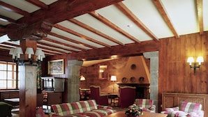 Amplia sala de estar con vigas de madera, chimenea y comedor con mesa y sillas de madera.