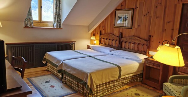 Un dormitorio acogedor con cabecera de madera, cama doble, mesita de noche con lámpara, una silla y un radiador.