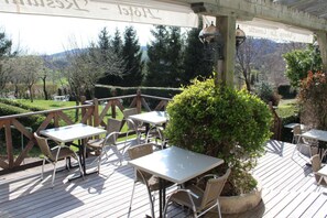 Un patio al aire libre con mesas y sillas, rodeado de vegetación y vistas al campo.