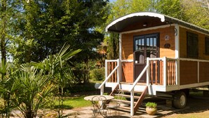 Una cabaña de madera con un porche, una mesa y sillas, rodeada de follaje.