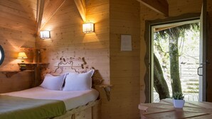 Habitación de cabaña de madera con una cama, una mesita y una ventana con vista a árboles.