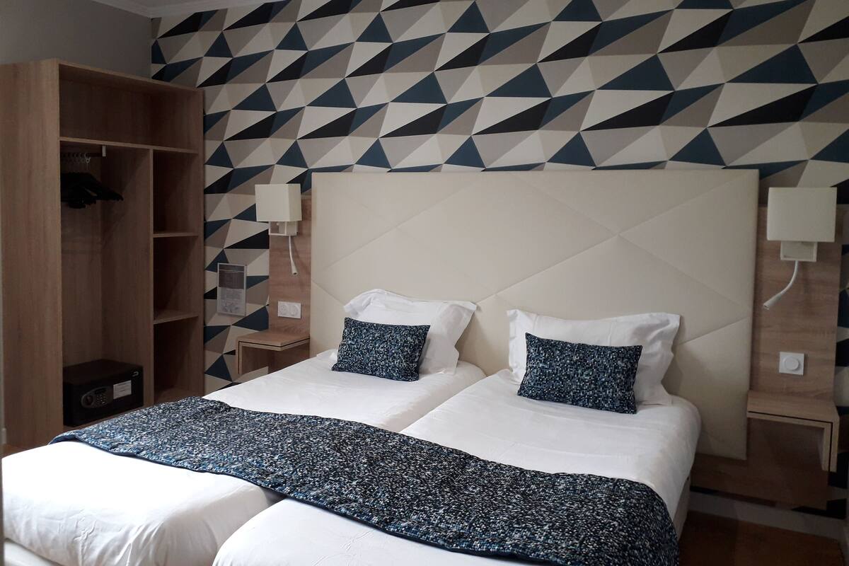 A double bed with a patterned bedspread, a wardrobe, and a geometric-patterned wall.