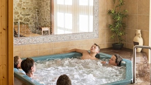 Un jacuzzi con cuatro personas, rodeado de paredes de piedra y paneles de madera.