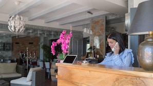 Un área de recepción con un mostrador de madera, una laptop y un jarrón con orquídeas rosadas. Se aprecia una pared de ladrillo y una lámpara colgante al fondo.