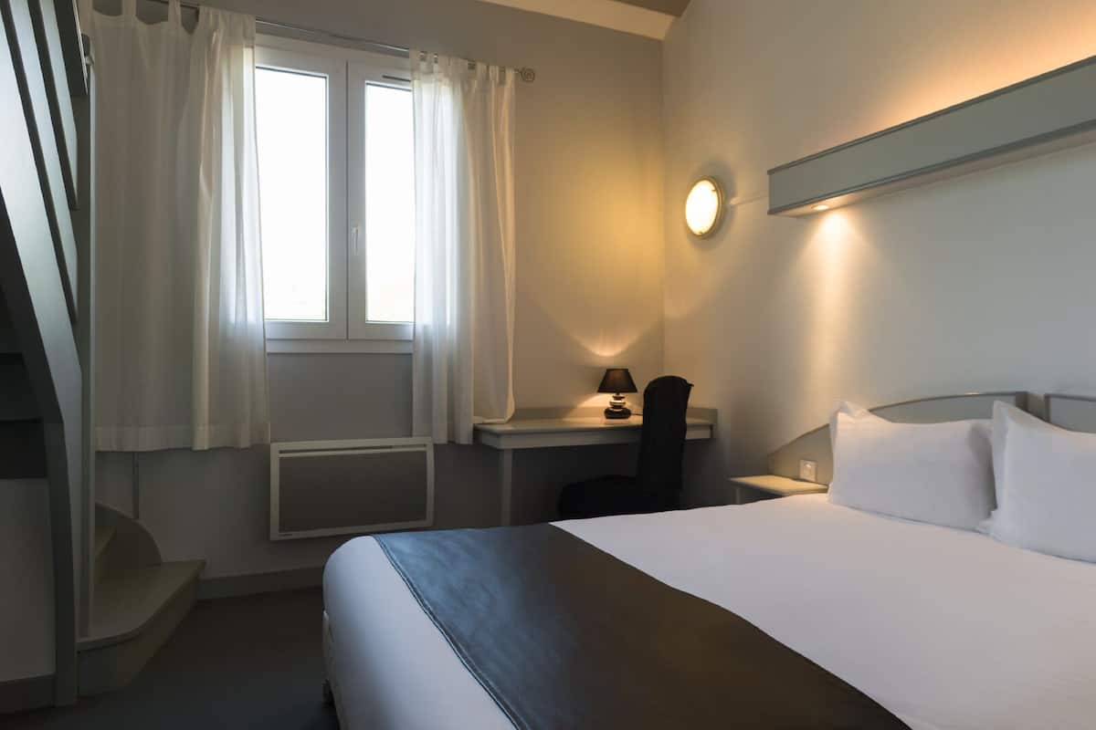 A hotel room with a bed, a desk, a chair, and a window with curtains.