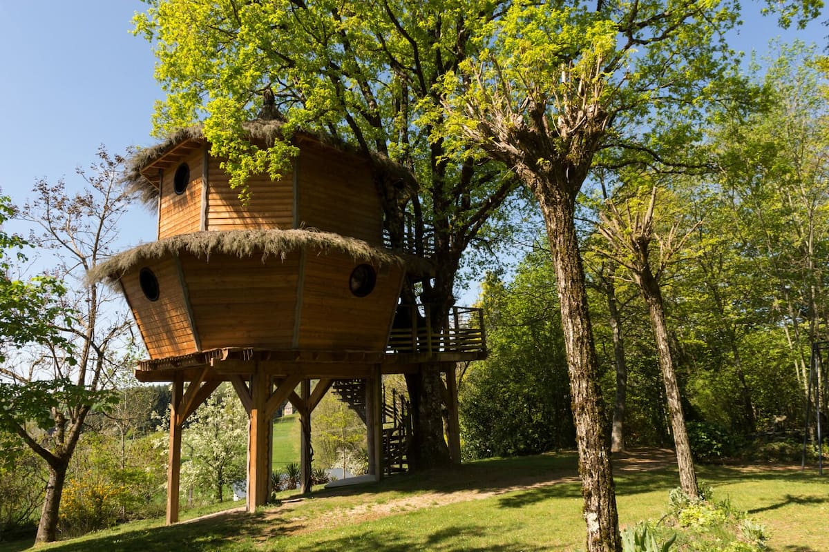 A treehouse with a thatched roof and wooden structure, surrounded by lush greenery and trees.