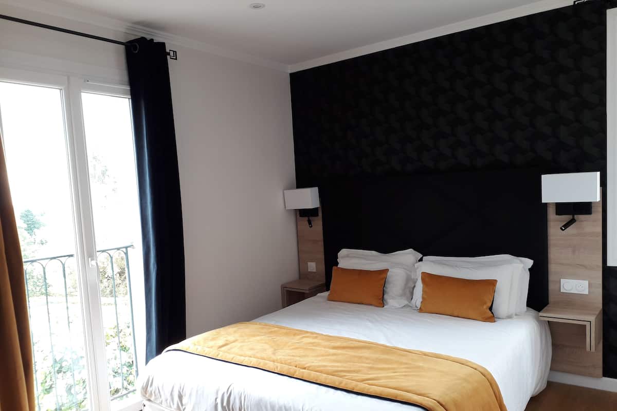 A hotel room with a large bed, two bedside tables, a black headboard, and a balcony with curtains.