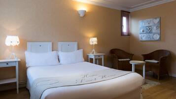 A neatly arranged hotel room with a large bed, two bedside tables with lamps, a small round table, two wicker chairs, and a decorative wall piece.