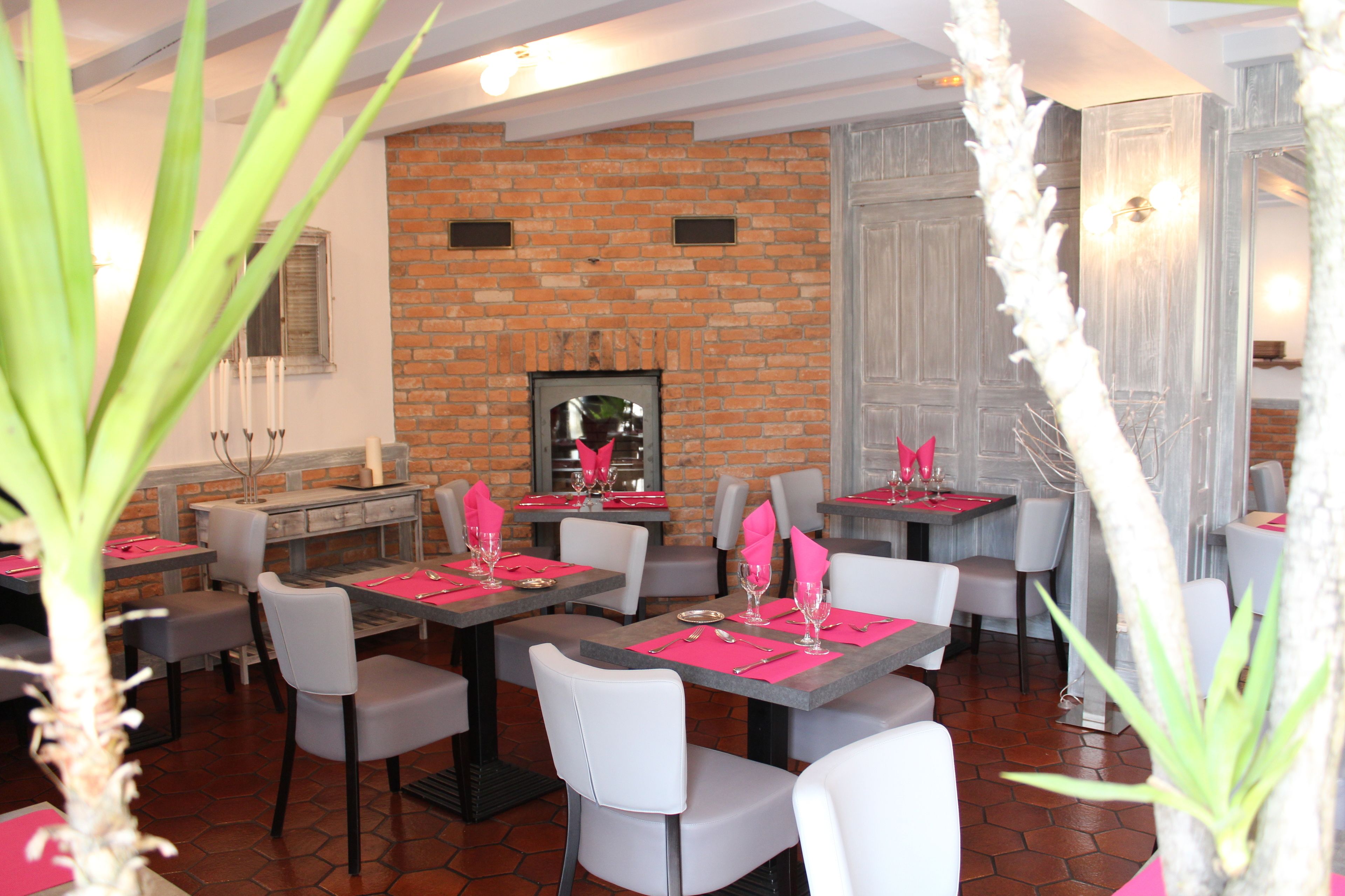 A restaurant with brick walls, white chairs, and tables set with pink napkins and silverware.