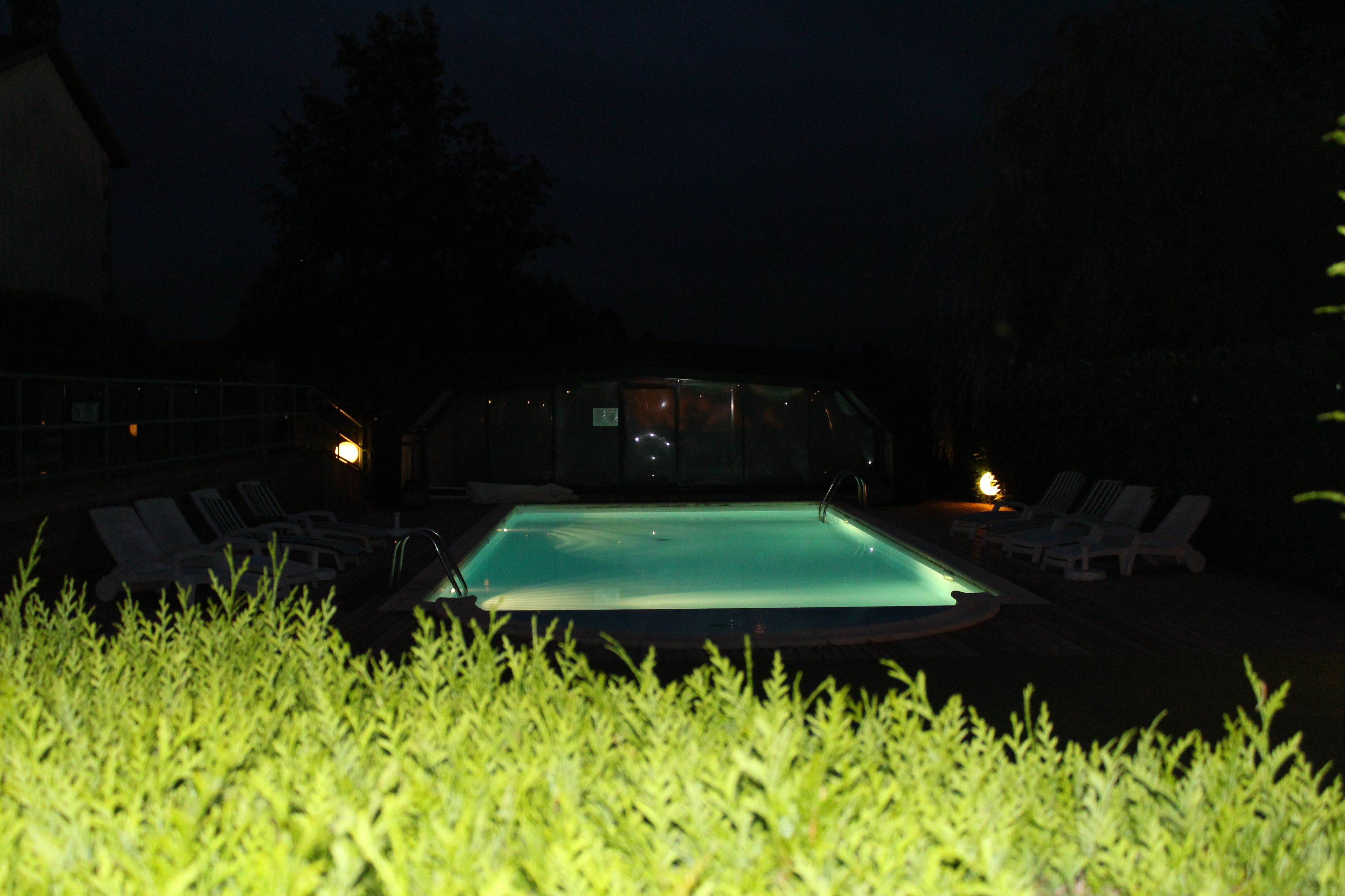 A swimming pool with lounge chairs and a glass enclosure in the background.
