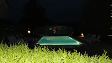 Una piscina con sillones de descanso y una estructura de vidrio al fondo.