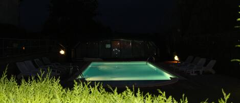 A swimming pool with lounge chairs and a glass enclosure in the background.
