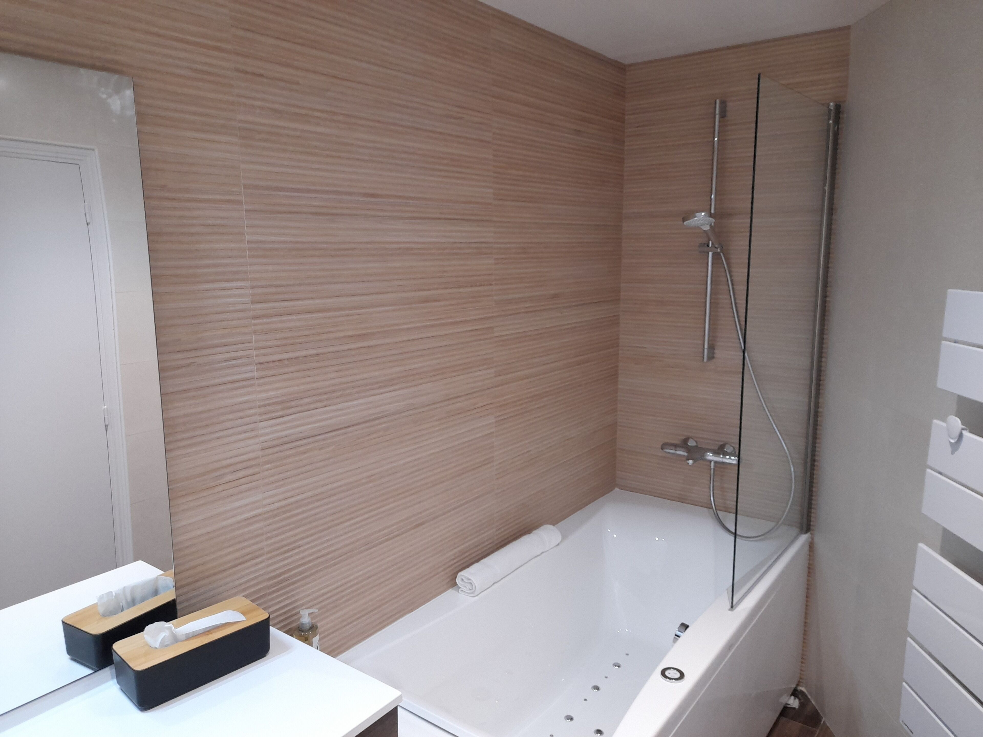 Un baño moderno con una pared de madera, una bañera blanca y una ducha con mampara de vidrio.
