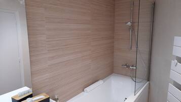 A modern bathroom with a wooden wall, a white bathtub, and a glass-enclosed shower.