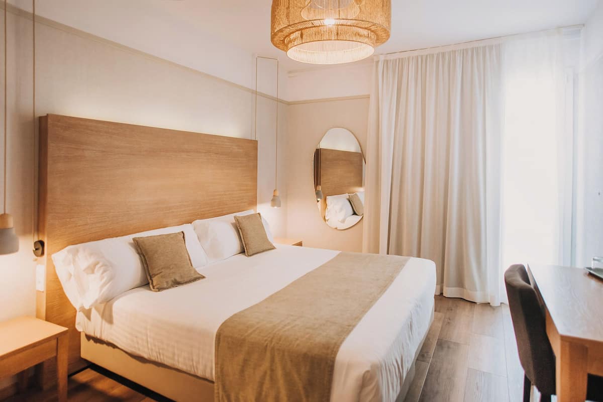 Una habitación de hotel con una cama grande, una mesita de noche, una silla, un escritorio, un espejo y una lámpara colgante.
