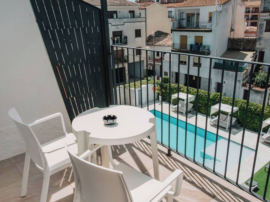 A balcony with a pool, white chairs, and a table.