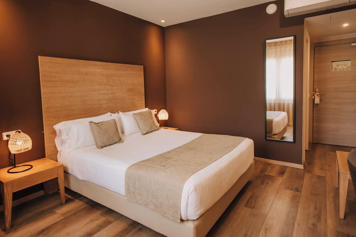 Un dormitorio ordenado con una cama grande, lámparas de noche, un cabecero de madera y un espejo en la pared.
