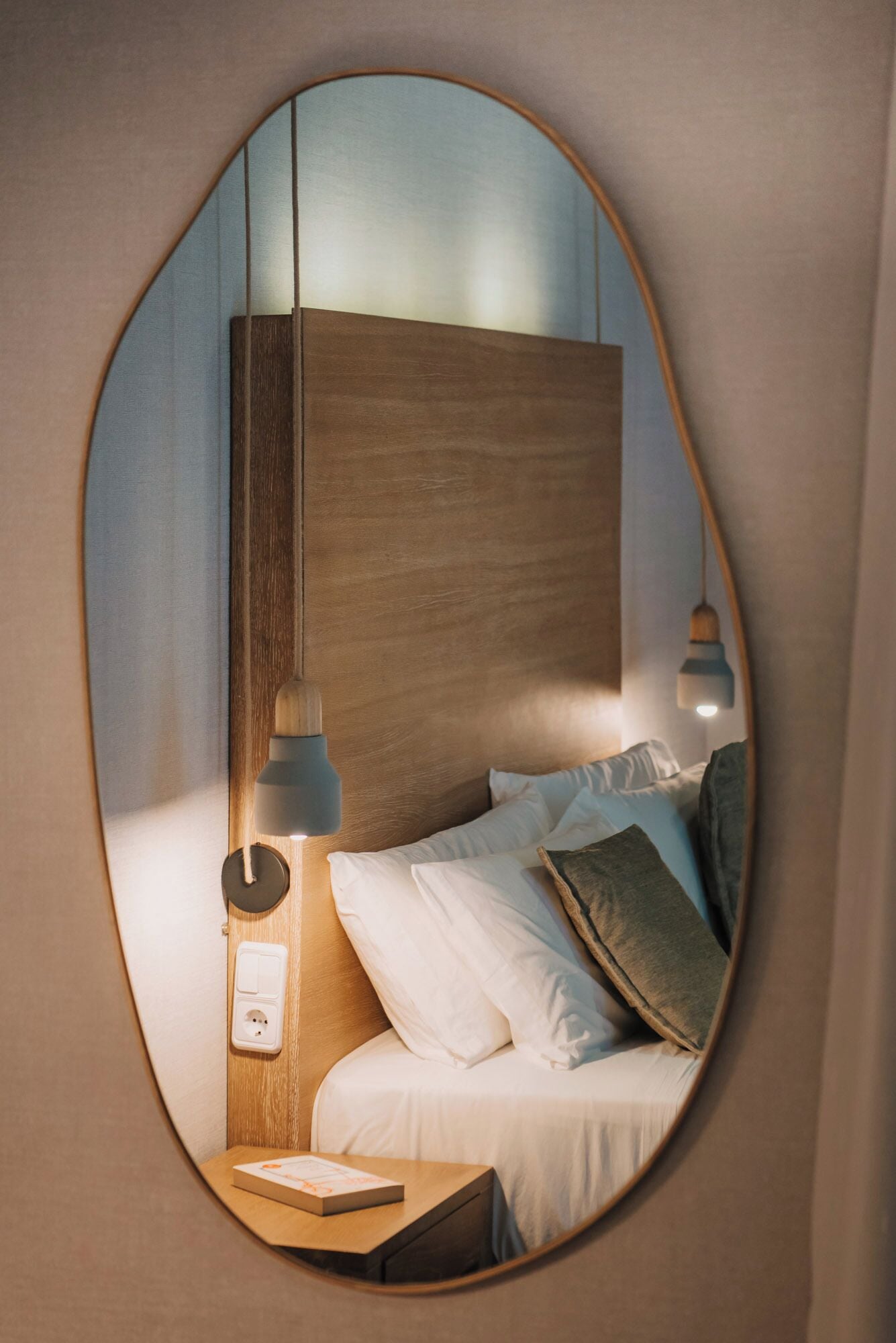 A bedroom with a wooden headboard, a bedside table with a lamp, and a bed with pillows.
