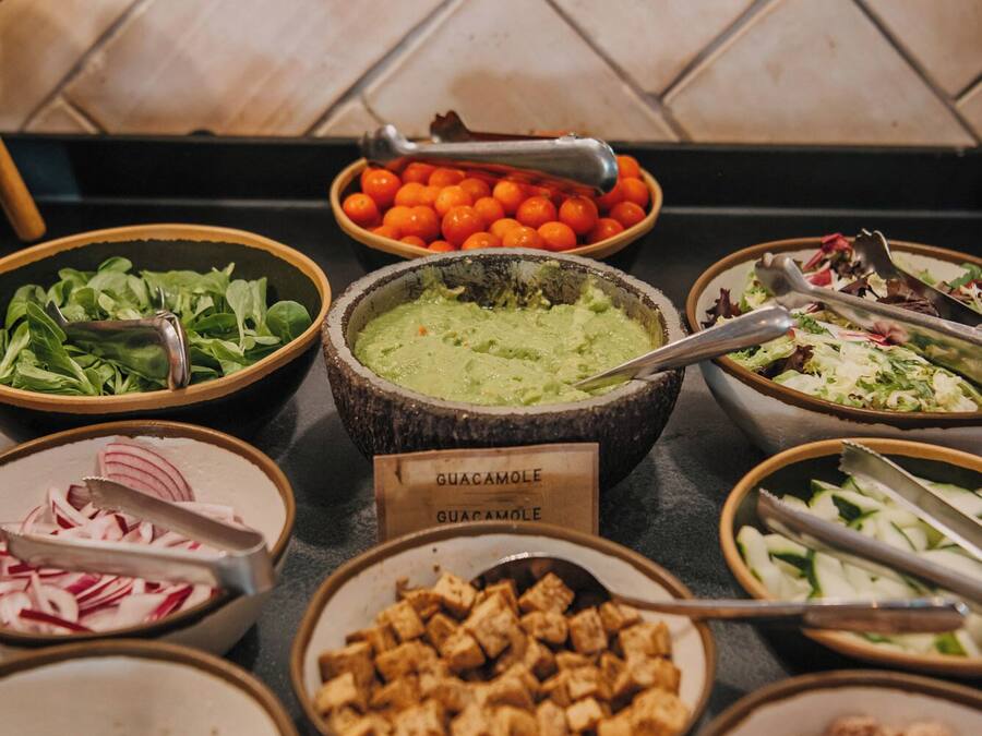 Un buffet proposant divers plats, notamment du guacamole, des salades et d’autres mets.