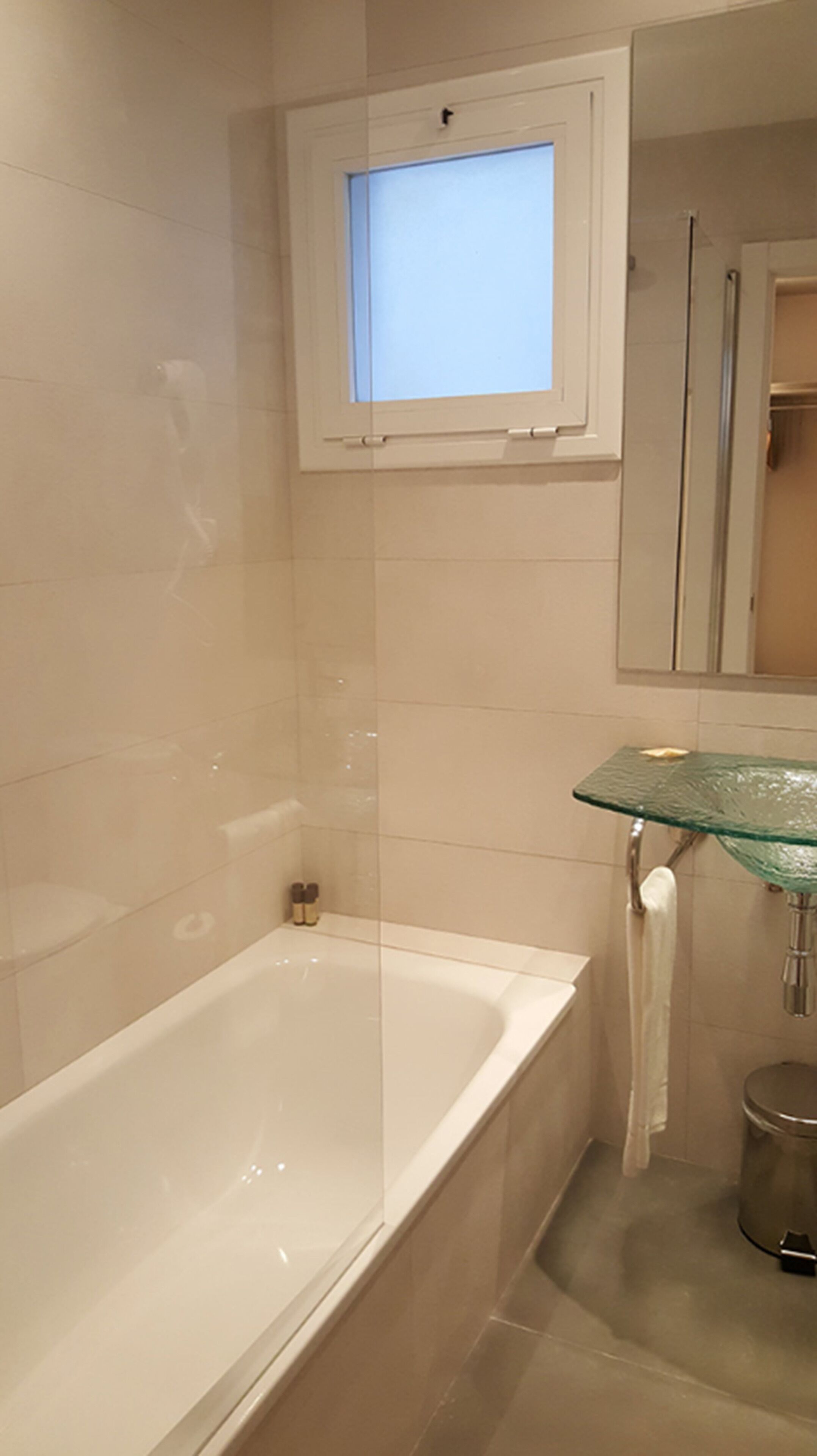 Un baño con bañera, estante de vidrio, espejo y ventana.