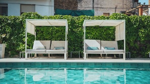 Zona junto a la piscina con dos sillas reclinables blancas bajo una pérgola, rodeada de abundante follaje verde.