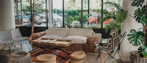 A cozy seating area with a cushioned sofa, wicker chairs, and a large window offering a view of parked cars and greenery outside.