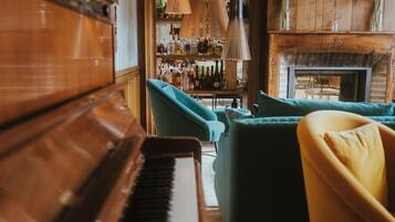 Un piano, butaques color turquesa, una zona de bar amb ampolles i una llar de foc.