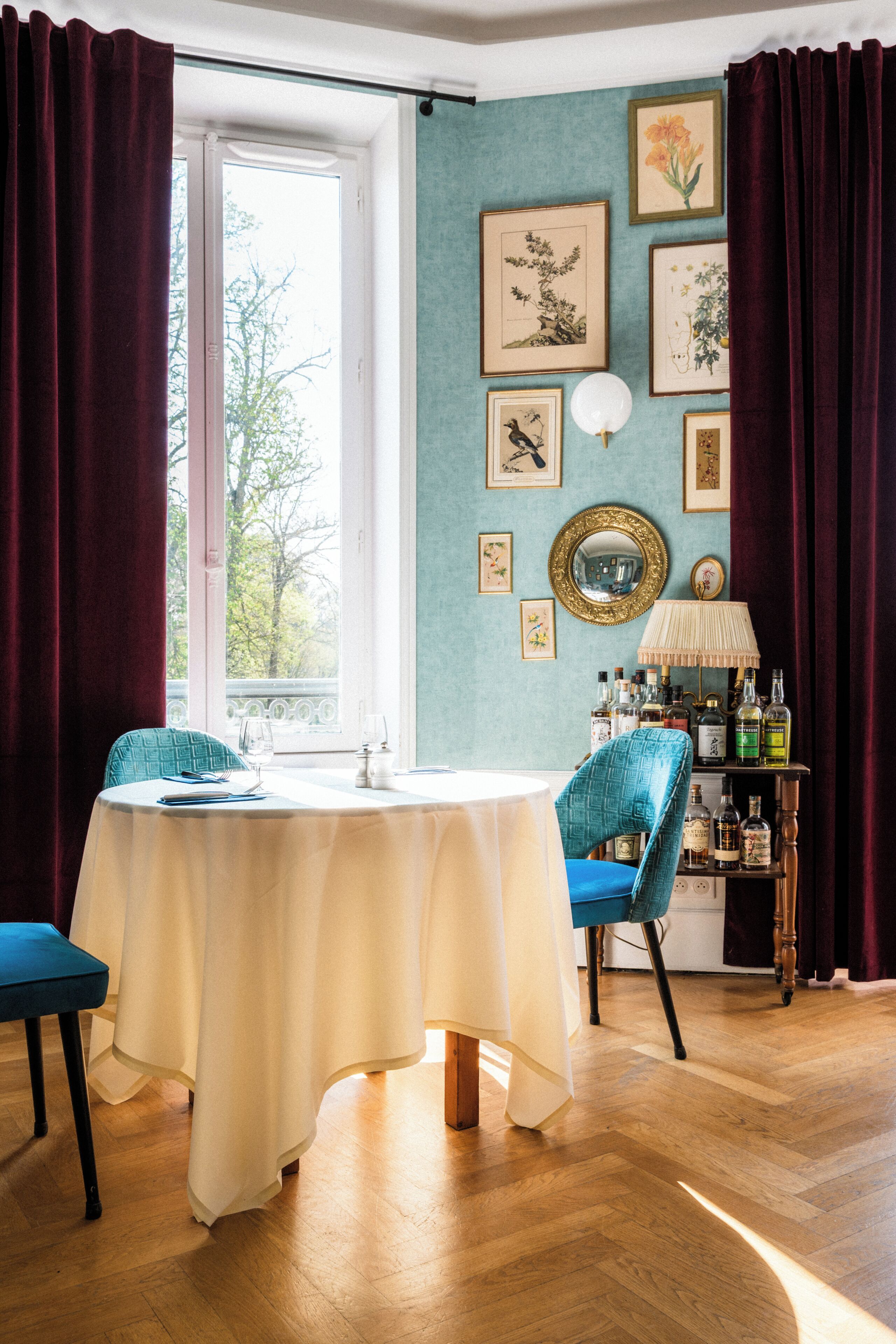 A room with a table, chairs, a window, and a wall with framed pictures and a mirror.