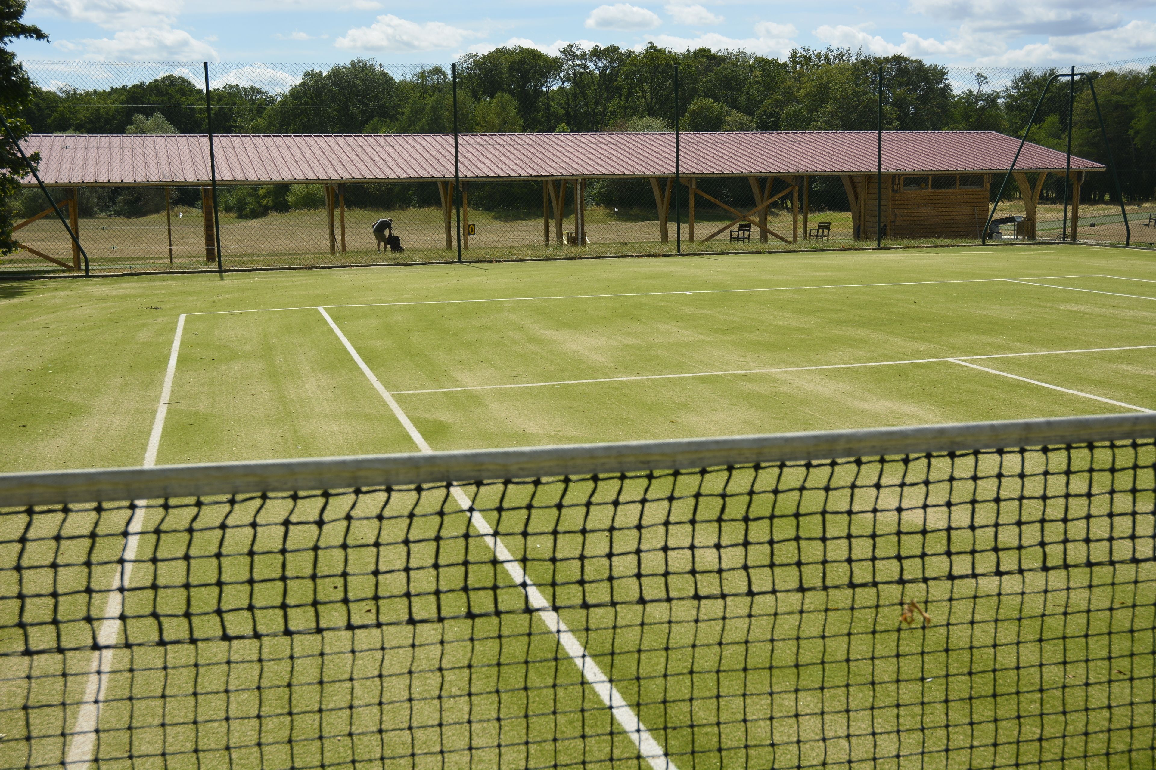 A tennis court with a net, a covered spectator area, and a wooden pavilion.