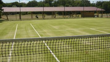 A tennis court with a net, a covered spectator area, and a wooden pavilion.