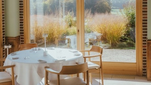 A dining area with a round table, chairs, and a view through large glass doors. - Domaine Et Golf Du Roncemay (Chassy)