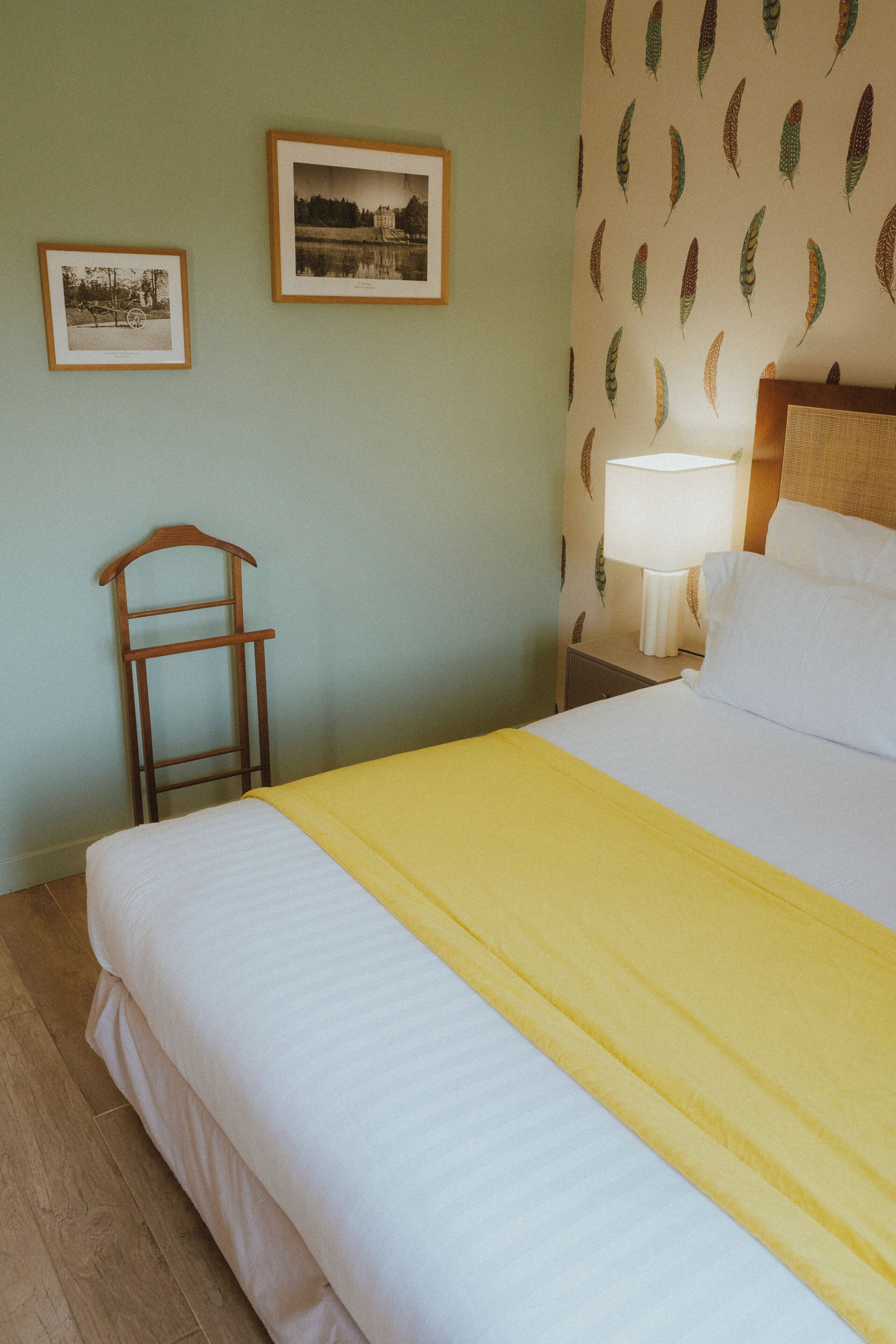 Un letto ben rifatto con copriletto giallo, una lampada da comodino e due quadri appesi alla parete.