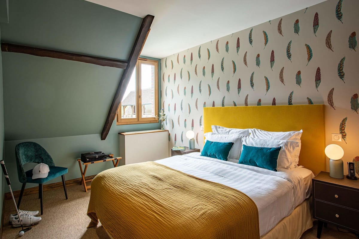 A bedroom with a bed, a chair, a desk, a lamp, and a window.