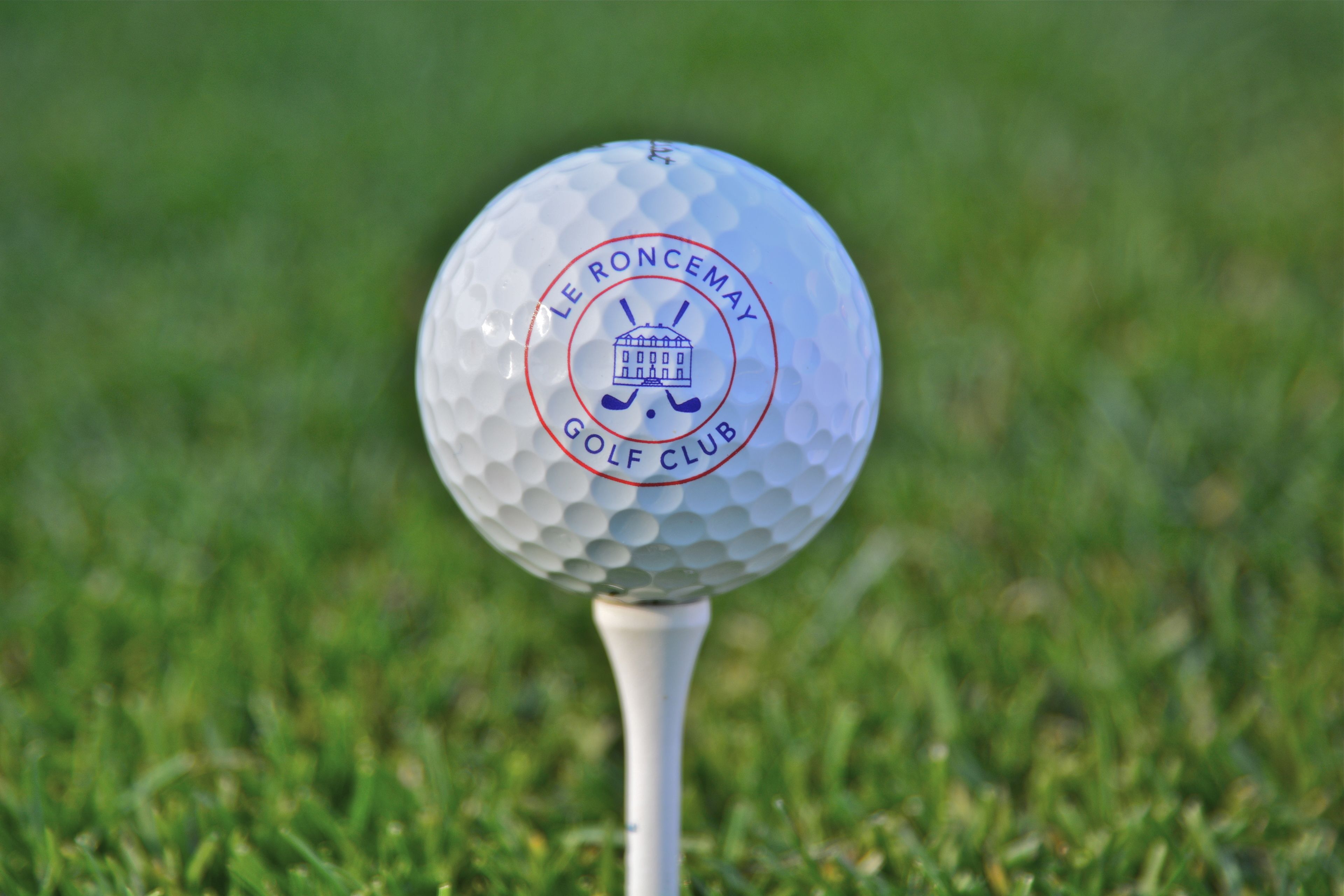 Una pelota de golf con el texto 'Le Roncemay Golf Club' sobre ella, colocada en un tee blanco.