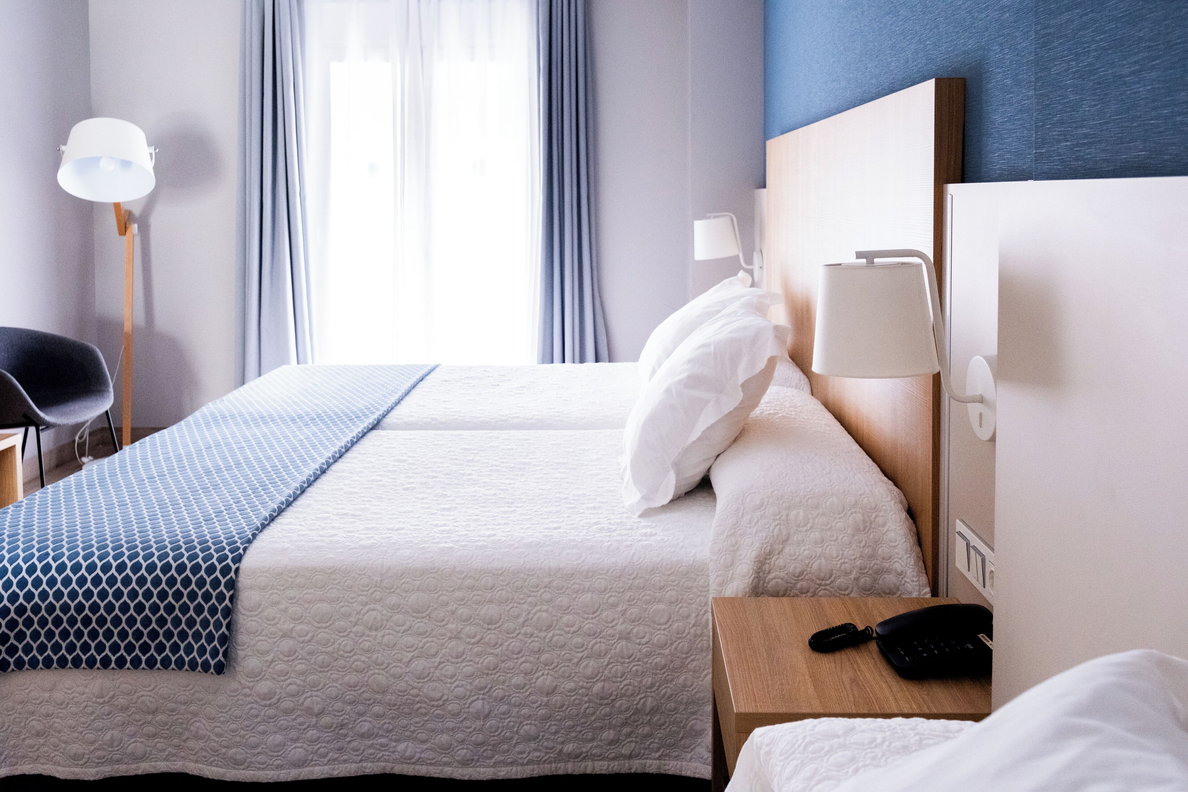 A hotel room with two beds, a desk with a lamp, a chair, and a phone on the nightstand.
