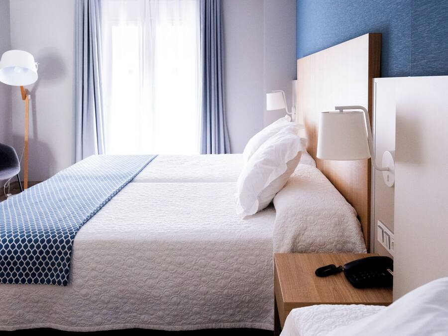 Habitación de hotel con dos camas, un escritorio con lámpara, una silla y un teléfono en la mesita de noche.