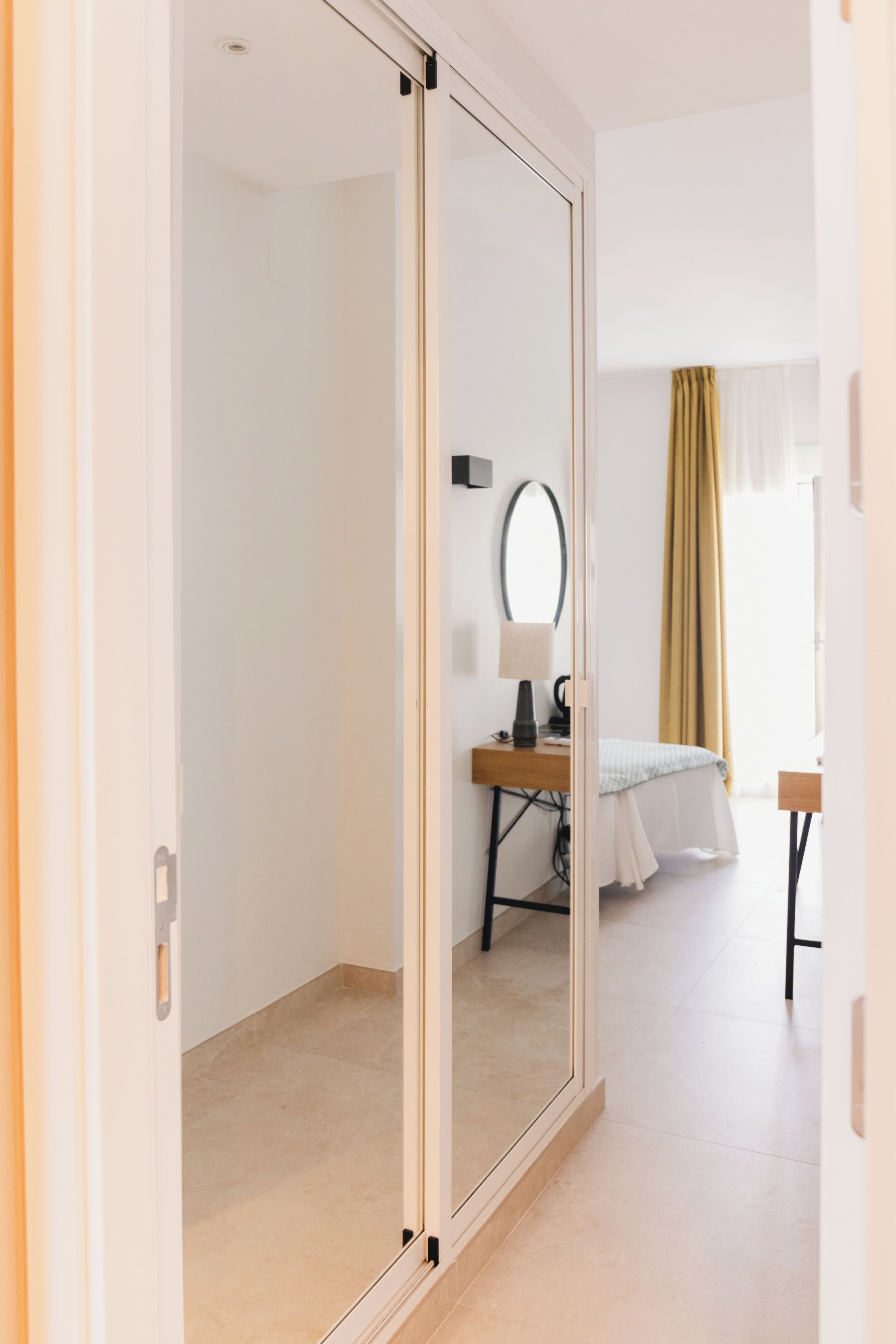 Habitación de hotel con puerta corrediza, una cama, un escritorio con lámpara y un espejo.