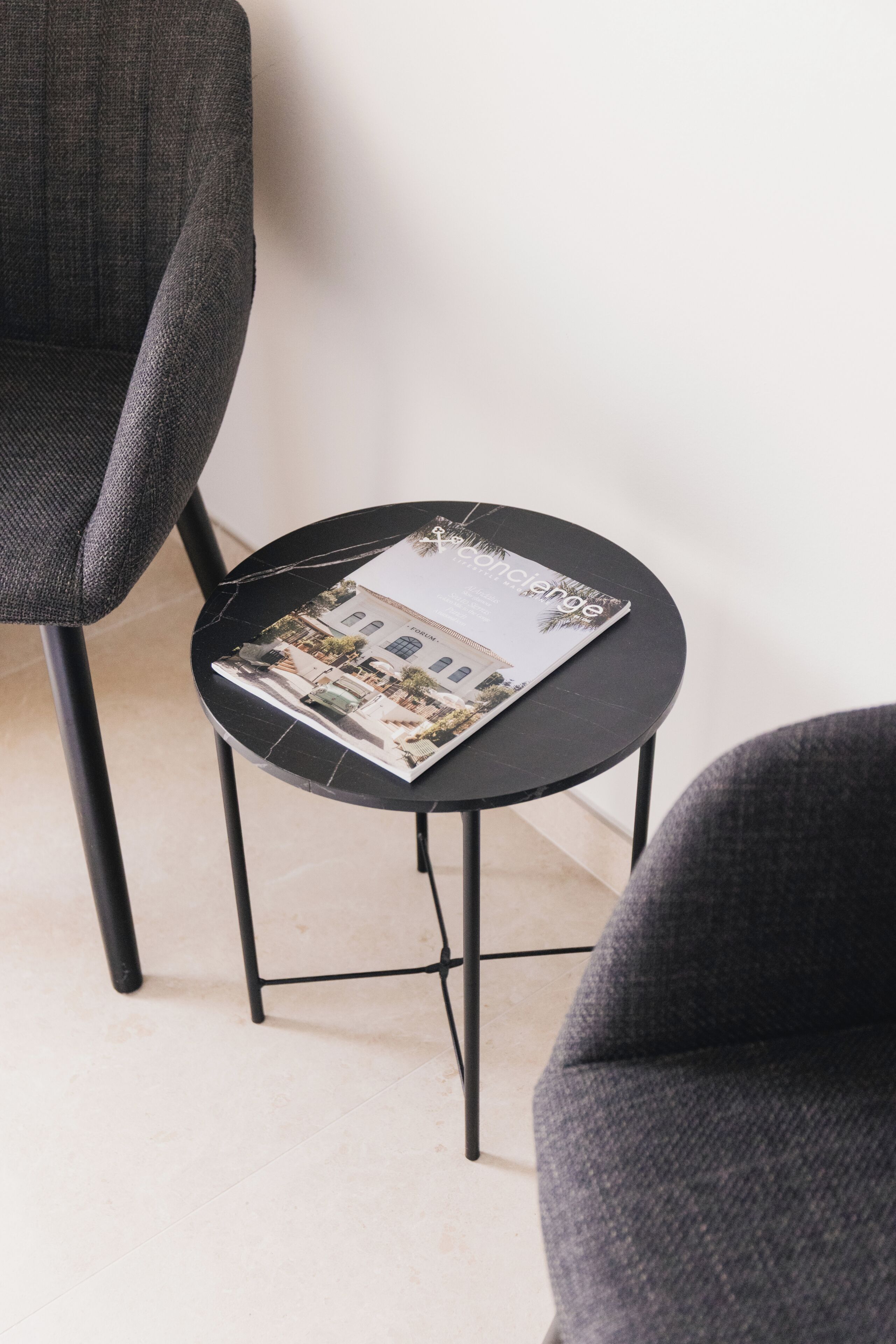 A small round table with a magazine on it, positioned between two grey chairs.