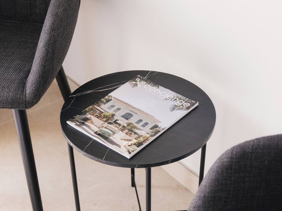 Una mesa redonda pequeña con una revista encima, ubicada entre dos sillas grises.