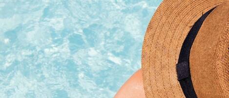 A person leaning over a pool edge, wearing a straw hat.