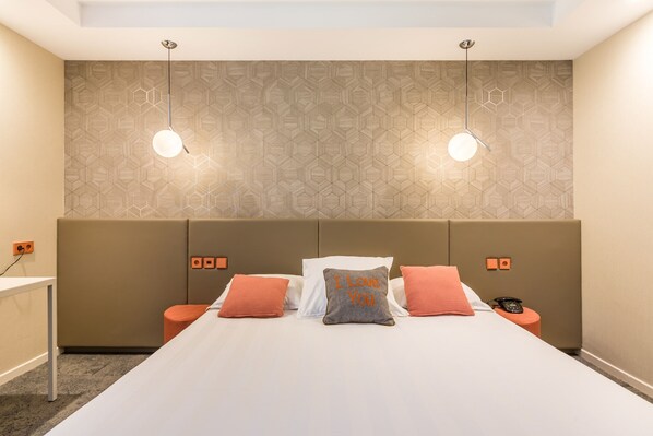 A hotel room with a bed, two nightstands, a desk, and a patterned wall.