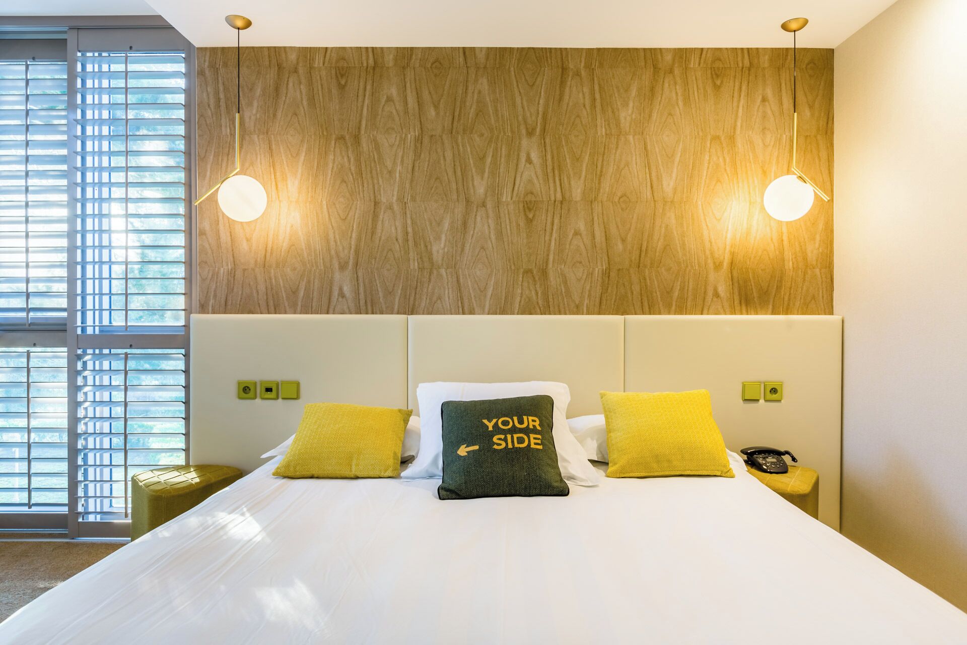 Una habitación de hotel moderna con una cama grande, dos lámparas de noche y un cabecero de madera.