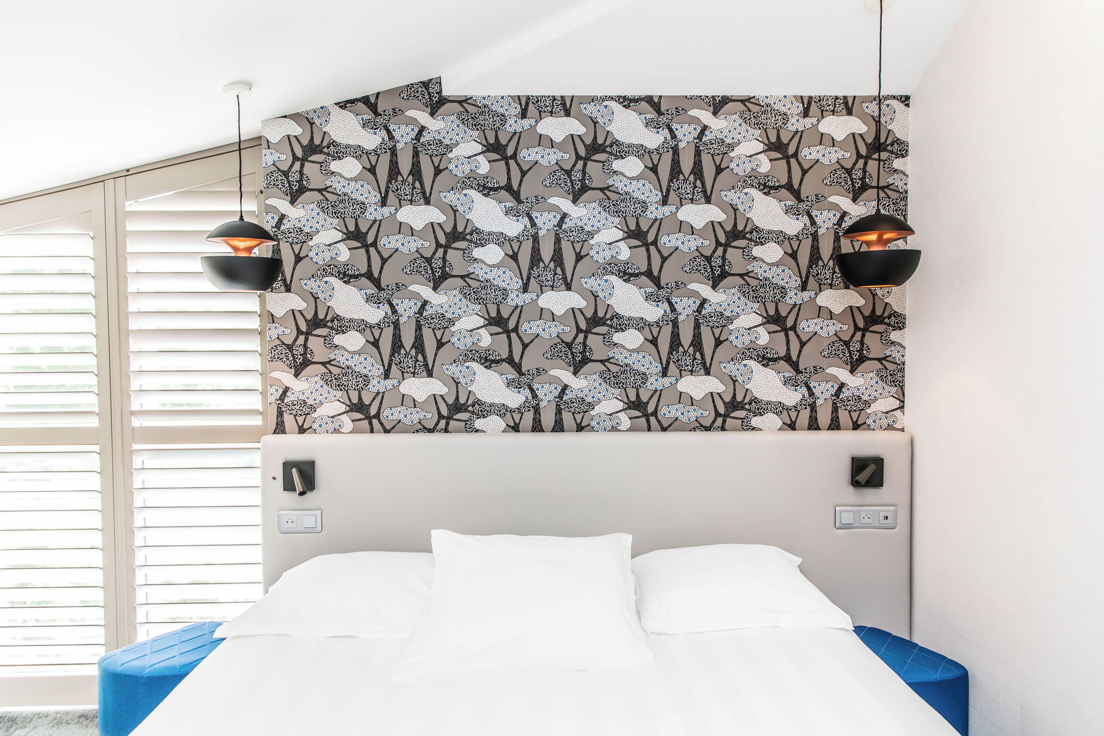 Une chambre avec un lit, un mur orné d’un motif floral et deux lampes suspendues.