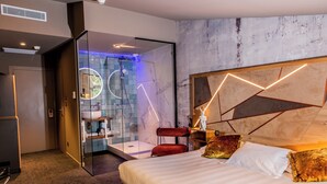 Een moderne hotelkamer met een groot bed, een douchecabine van glas, een rode stoel en een geometrisch hoofdeinde.