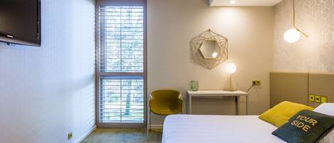 Une chambre d’hôtel équipée d’un lit, d’un bureau, d’une chaise, d’une télévision et d’une fenêtre avec des stores.