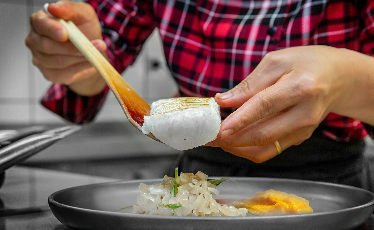 Una persona sosteniendo comida con palillos sobre un plato de arroz y otros ingredientes.