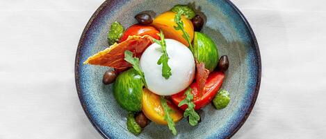 A plate with a poached egg, tomatoes, olives, and greens.