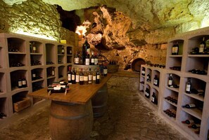 A wine cellar with wooden barrels, shelves of wine bottles, and a stone wall.