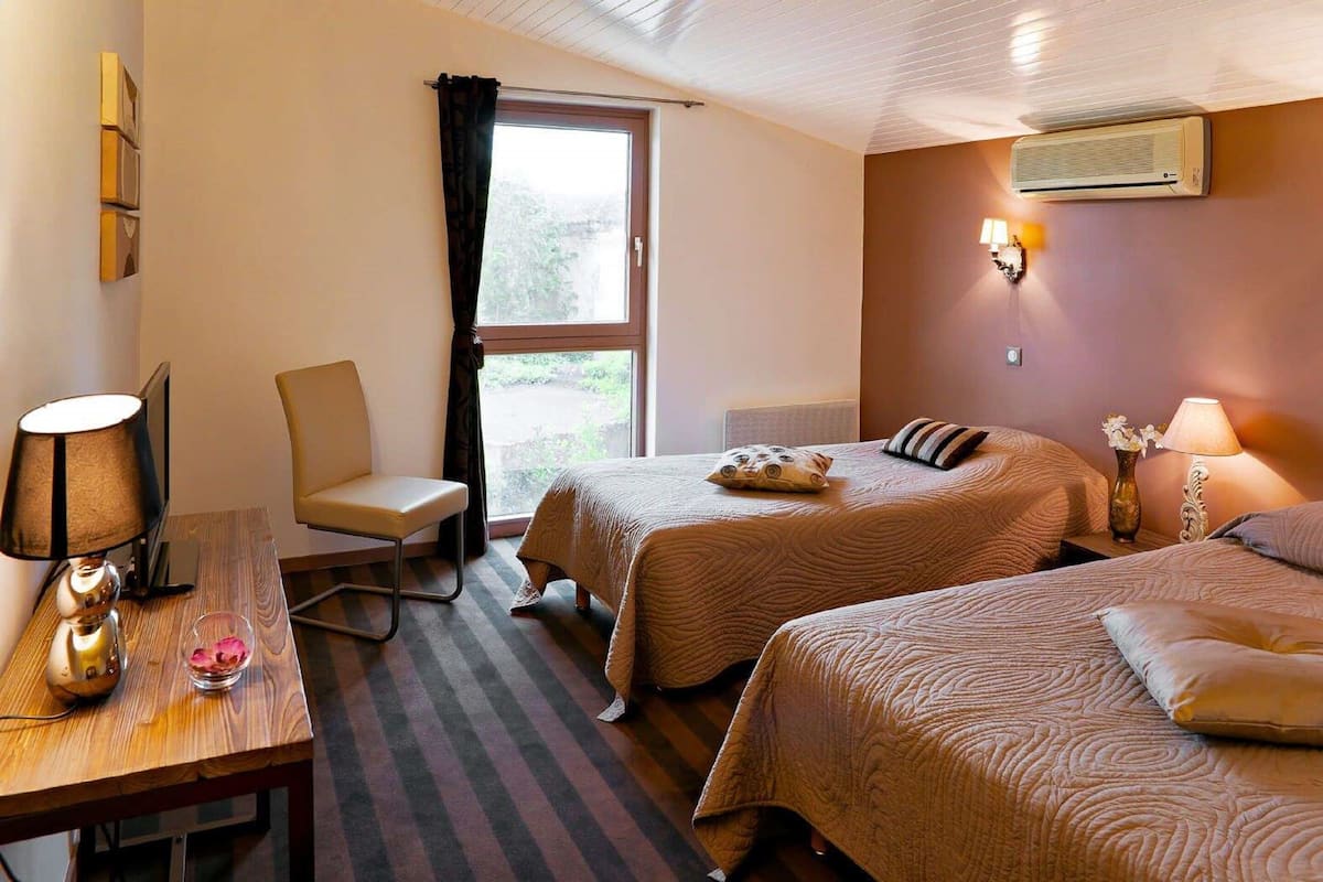 Une chambre d’hôtel avec deux lits, un bureau avec une lampe, une chaise et une fenêtre avec des rideaux.